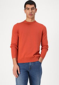 Suéter laranja tricotado com gola redonda e punhos canelados, combinado com jeans de denim azul claro. Textura suave, design ajustado e sem padrões visíveis.
