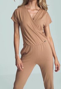 Combinaison beige style portefeuille avec manches courtes, encolure en V et taille élastique. Tissu doux à texture lisse et jambes ajustées.