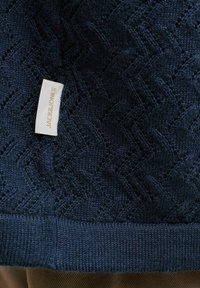 Tissu tricoté bleu foncé avec un motif chevron et une petite étiquette blanche portant la mention "JACK&JONES" cousue près du bord inférieur.