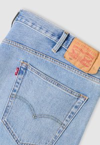 Φωτεινό γαλάζιο τζιν παντελόνι με πίσω τσέπη, πορτοκαλί ραφές, θηλιά για ζώνη, κόκκινη ετικέτα Levi's και φθαρμένη καφέ δερμάτινη ετικέτα της μάρκας Levi Strauss & Co.