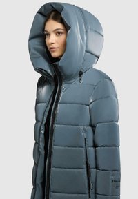 Giubbotto imbottito con cappuccio in una tonalità di blu tenue, caratterizzato da una finitura lucida, un grande cappuccio e una chiusura con zip nera, dotato di tasche laterali.