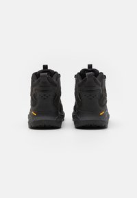 Czarne buty trekkingowe z teksturowanym materiałem, wzmocnionym piętą i pomarańczowym logo Vibram. Posiadają pętle do zakupu i liczne otwory wentylacyjne.