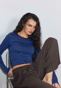 Top a maniche lunghe a righe blu e nere abbinato a pantaloni a gamba larga marroni a righe sottili. Il tessuto sembra morbido, con una silhouette aderente.