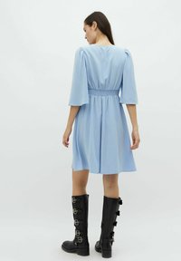 Rochie bleu deschis cu mâneci până la cot, talie smocking și fustă evazată; purtată cu cizme negre pana la genunchi cu detalii din curea.