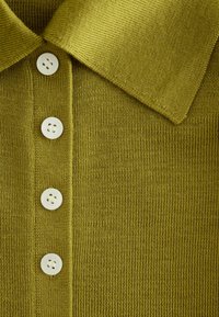 Tissu tricoté vert avec un col et quatre boutons ronds blancs alignés verticalement au centre.