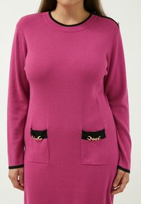 Abito a maniche lunghe fucsia con texture a coste, caratterizzato da tasche nere con dettagli in catena dorata e finitura del collo nera uniforme.
