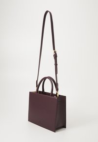 Sac à main structuré en cuir bordeaux foncé. Présente des anses supérieures doubles, une bandoulière amovible et des accessoires en métal doré.