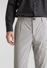 Šedé kostkované kalhoty s jemnou texturou, se striktními sklady a zapínáním na knoflík, spárované s tmavě květinovým vzorem na košili.
