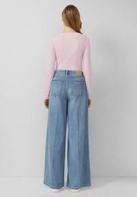Jasnoróżowa bluzka z długim rękawem w połączeniu z niebieskimi dżinsami o wysokim stanie i szerokich nogawkach. Klasyczne tylne kieszenie i subtelna faktura materiału.
