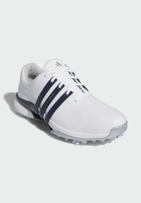 Bílé golfové boty s hladkým koženým svrškem, třemi tmavě modrými pruhy a průhlednou gumovou podrážkou s malými trakčními hroty.