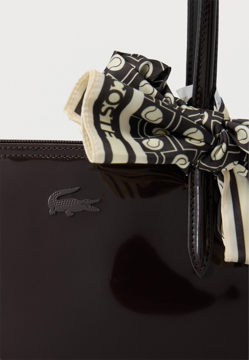 Glossy black handbag with embossed crocodile logo and black-and-white patterned scarf tied to handle.