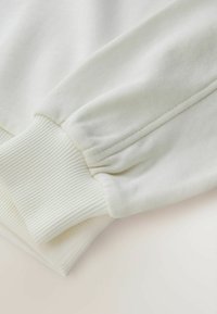 Manche de sweat-shirt beige clair, avec un bord-côtes, une texture douce et un tissu lisse avec des détails de couture subtils.