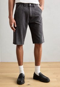 Svarta denimshorts med avslappnad passform, fem fickor och synlig s�ömnad. I kombination med svarta loafers och vita strumpor.