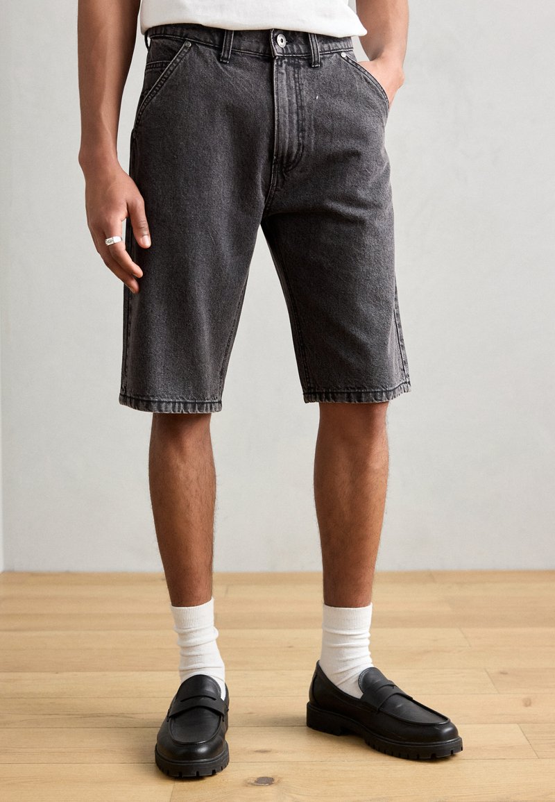 Shorts in denim nero con una vestibilità comoda, cinque tasche e cuciture in evidenza. Abbinati a mocassini neri e calzini bianchi.