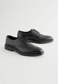 Chaussures habillées en cuir noir avec une finition texturée, un laçage, un bout rond et une semelle lisse. Coutures discrètes le long des bords.