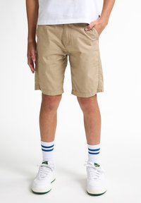 Pantalones cortos caqui, de tela de algodón, con corte recto, bolsillos laterales, combinados con zapatillas blancas y calcetines a rayas azules. Diseño simple y casual.
