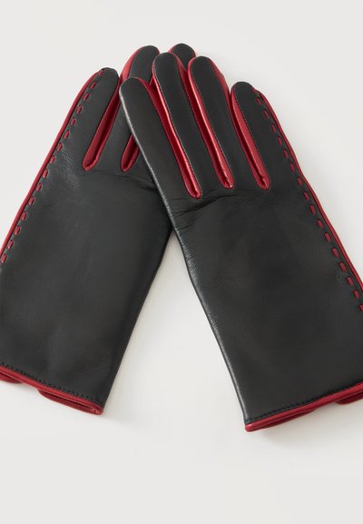 Gants en cuir noir avec bordure rouge et détails de couture, doigts entièrement couverts, posés à plat sur une surface blanche.