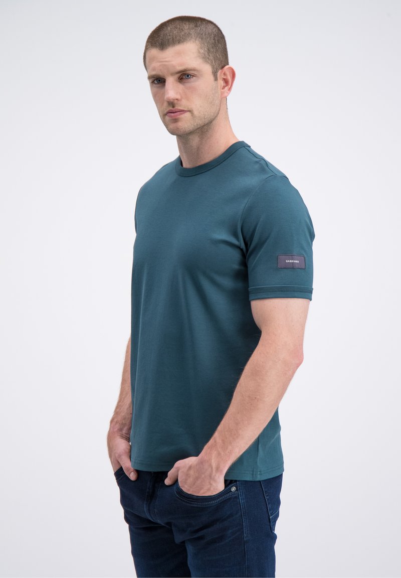 Žalsvai mėlyna trumpomis rankovėmis medvilninė marškinėliai su apvalia iškirpte. Kairėje rankovėje yra aplikacija su etikete. Lygus tekstūra.