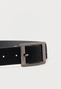 Must nahast vöö tekstuurse viimistlusega, millel on ristküliku kujuline metallist pannal ja viis kinnitusauku. Sile sisepind.