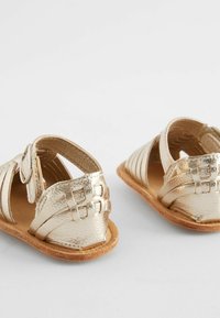 Goldene metallische Sommerschuhe mit geflochtenen Riemen, verstellbarem Schnallenverschluss und brauner strukturierter Sohle. Offenes Design im rutschfesten Stil.