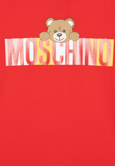 Crvena pamučna majica s grafikom medvjeda koji proviruje preko riječi "MOSCHINO" u podebljanim bijelim i žutim slovima. Glatka tekstura.