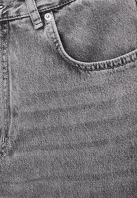 Primer plano de un bolsillo de jeans de mezclilla gris con costura visible, presilla para el cinturón y botón de remache metálico.