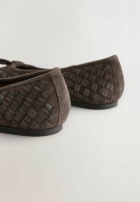 Barna szarvasbőr balettcipő, oldalán szövött bőr részletekkel és lapos gumitalppal. Lekerekített orr kialakítás.