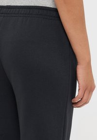 Pantaloni jogger grigi scuri con vita elasticizzata, realizzati in un morbido tessuto misto cotone. L'attenzione è posta sulla posizione laterale e delle mani.