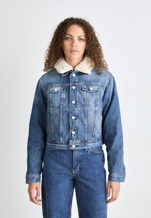 Chaqueta de denim de diseño recortado, color azul claro, y cuello de borreguillo blanco; cuenta con dos bolsillos en el pecho y cierre frontal de botones.