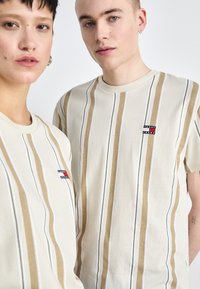 T-shirts en coton avec des rayures verticales beige et blanches, avec un petit logo sur la poitrine. Design à manches courtes et col rond.