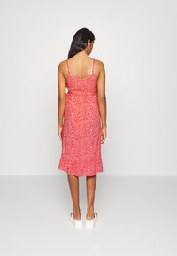 Vestido midi floral vermelho com alças finas, bainha rodada e cintura ajustada. Textura de tecido suave e padrão floral branco pequeno por toda a peça.