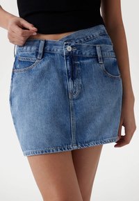 Jupe en denim bleu moyen avec une légère décoloration, dotée d'une taille ajustée, de poches avant et d'une fermeture à bouton pour un enfilage facile.