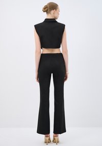 Top nero cropped senza maniche con colletto abbinato a pantaloni neri a vita alta e svasati; tessuto liscio e design minimalista.