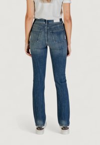 Jeans acampanados de color azul oscuro, hechos de denim, con una cintura alta, dos bolsillos traseros y una textura desgastada cerca del dobladillo.