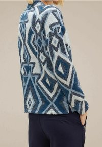 Neuletakki, jossa on geometrinen kuvio sinisen ja valkoisen sävyissä, rento malli ja tekstuurinen kangas.