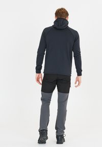 Mörkgrå hetjacka med långa ärmar, kombinerad med tvåfärgade byxor: svart ovan, grå nedan, och svarta vandringsskor.