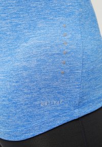 Blaues Dri-FIT-Shirtmaterial mit einer melierten Textur und fünf grauen Punkten auf der Seite, mit einem sichtbaren Dri-FIT-Logo nahe dem Saum.