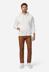 Witte hoodie met een voorzak, gecombineerd met bruin leren broeken, afgewerkt met witte sneakers. Eenvoudig design, zachte textuur en een relaxed fit.