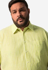 Camicia a righe verde chiaro realizzata in un tessuto leggero. Presenta una chiusura con bottoni nella parte frontale e una tasca sul petto.
