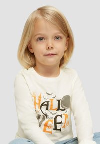 Helle, langärmelige T-Shirt mit einem Halloween-Motiv in Schwarz und Orange, ergänzt durch zusätzliche dekorative Elemente.