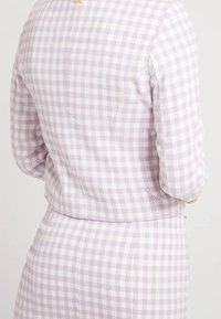 Chaqueta de cuadros lavanda con un corte ajustado, mangas largas y una textura suave. Acento de hardware en tono dorado en el escote.