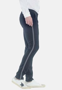 Pantaloni neri aderenti, con una striscia grigia verticale lungo il lato, abbinati a sneakers bianche con un accento di stella nera.