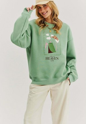 Zielona, oversize'owa bluza wykonana z mieszanki bawełny, z zabawnym nadrukiem przedstawiającym chmury, tygrysa oraz słowo "HEAVEN" napisane czarnym kolorem.