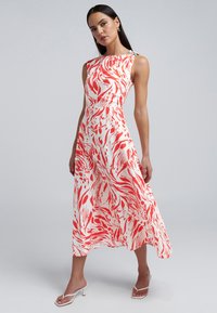 Floral midi-jurk met een witte basis en gedurfde rode en koraalkleurige abstracte patronen. Zachte stof, mouwloos ontwerp en een schouderaccent.