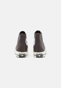 Brown leather high-top sneakers with white rubber soles, featuring a circular logo patch and black branding on the heel.