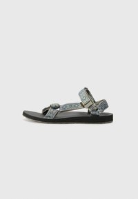 Blå mønstrede sandaler med tekstilremmer, gummisåler og flad design. Har knuder på remmene og en teksturert såle.