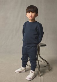 Ensemble sweat-shirt et jogger bleu marine en tissu doux, avec poignets côtelés et coupe décontractée, associé à des baskets blanches.