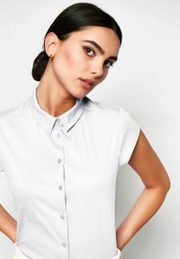Weißes kurzärmliges Button-Up-Hemd mit Kragen, das eine glatte Textur, einen dezenten Glanz und kleine Knöpfe entlang der Vorderseite aufweist.
