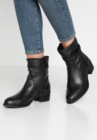 Bottines en cuir noir avec un design décontracté, fermeture éclair latérale et un petit talon empilé. Surface texturée avec une finition lisse.
