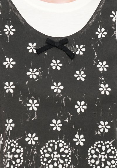 Zwarte tanktop met een witte bloemenprint, een gestructureerd oppervlak en een klein zwart strikdetail bij de halslijn.